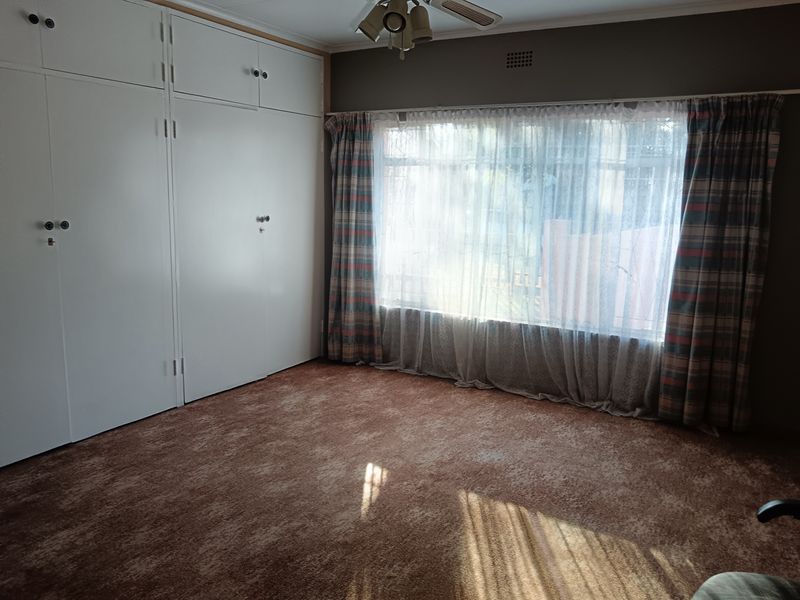 A spacious bedroom featuring extensive built-in cupboards, a ceiling fan, and carpeted flooring, offering a blank canvas for potential updates.