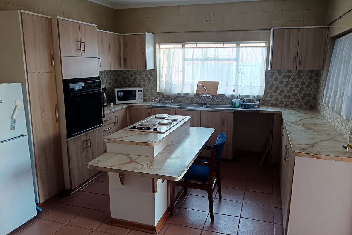 A functional kitchen featuring light wood-finish cabinetry, laminate countertops, a central island with a hob, and tiled flooring throughout.