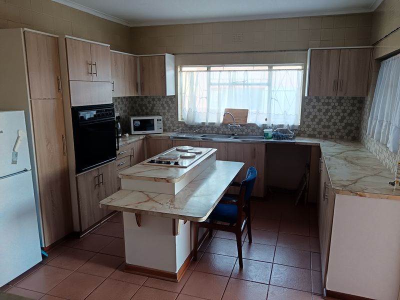 A functional kitchen featuring light wood-finish cabinetry, laminate countertops, a central island with a hob, and tiled flooring throughout.