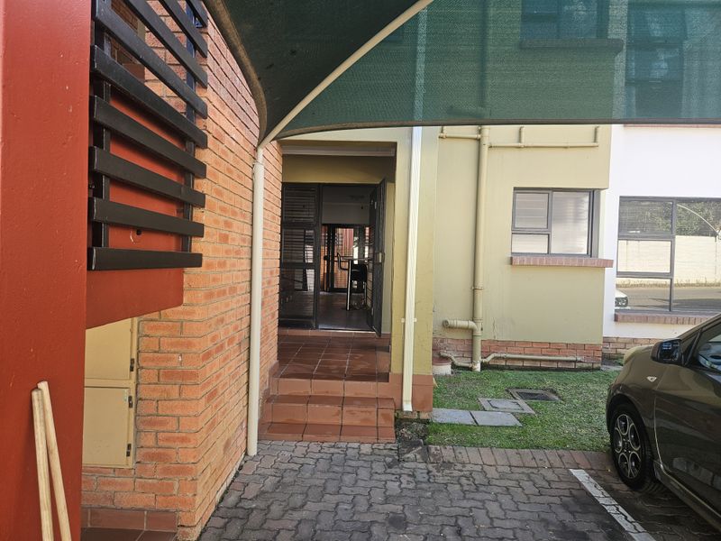 Front entrance of the townhouse featuring a paved driveway, shade sail, and tiled steps leading to the main security door.