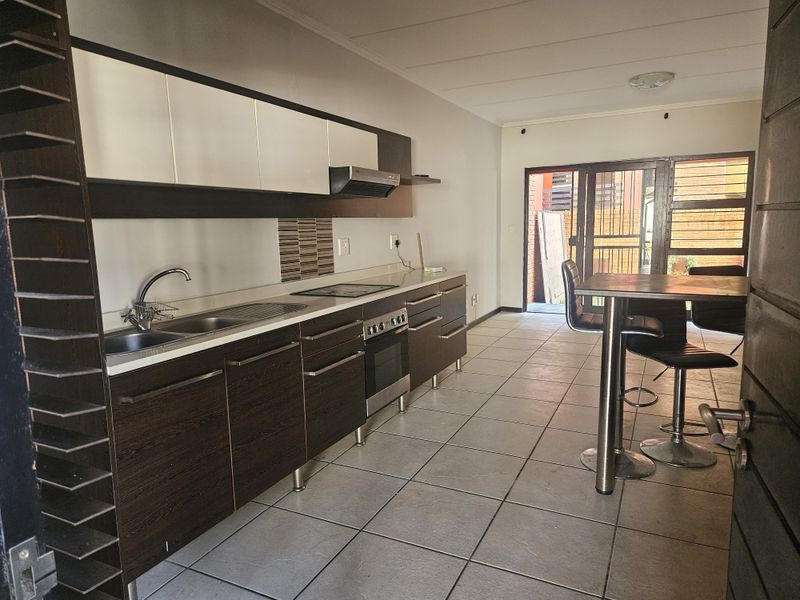 Open-plan kitchen featuring dark wood cabinetry, integrated appliances, and tiled flooring, leading directly to an outdoor patio area through sliding glass doors.