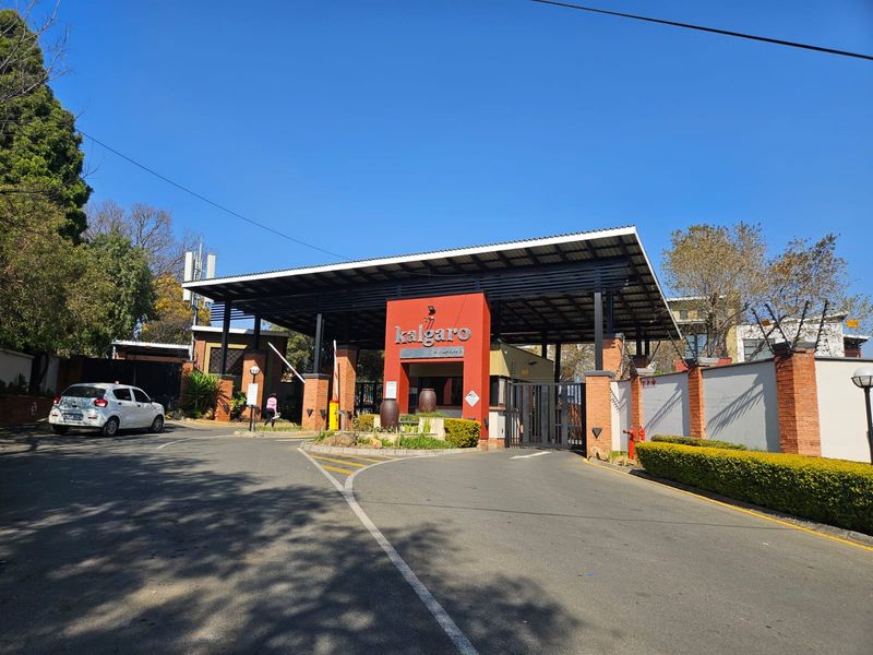 The main entrance and security gatehouse of the Kalgaro townhouse complex, featuring brick masonry, metal roofing, and controlled access infrastructure.
