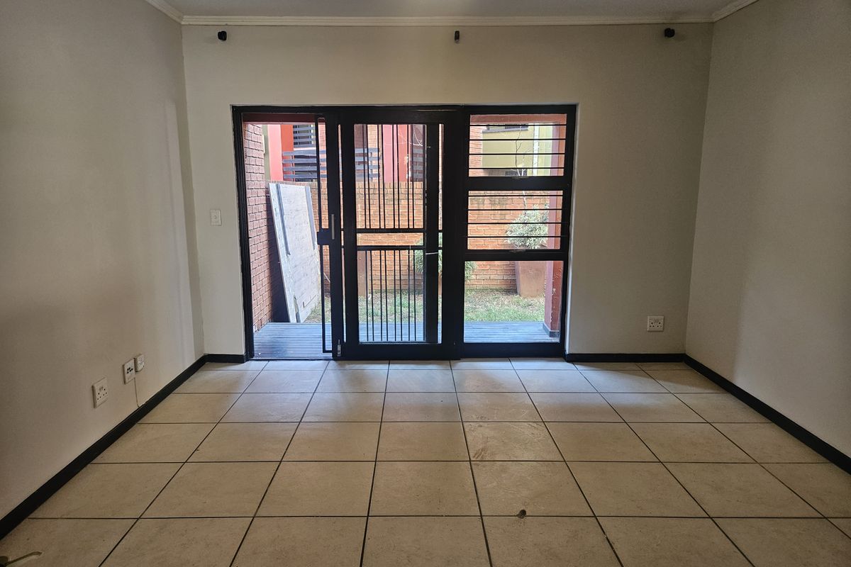 An empty living room featuring neutral tiled flooring and a secure sliding door providing direct access to the rear patio area.