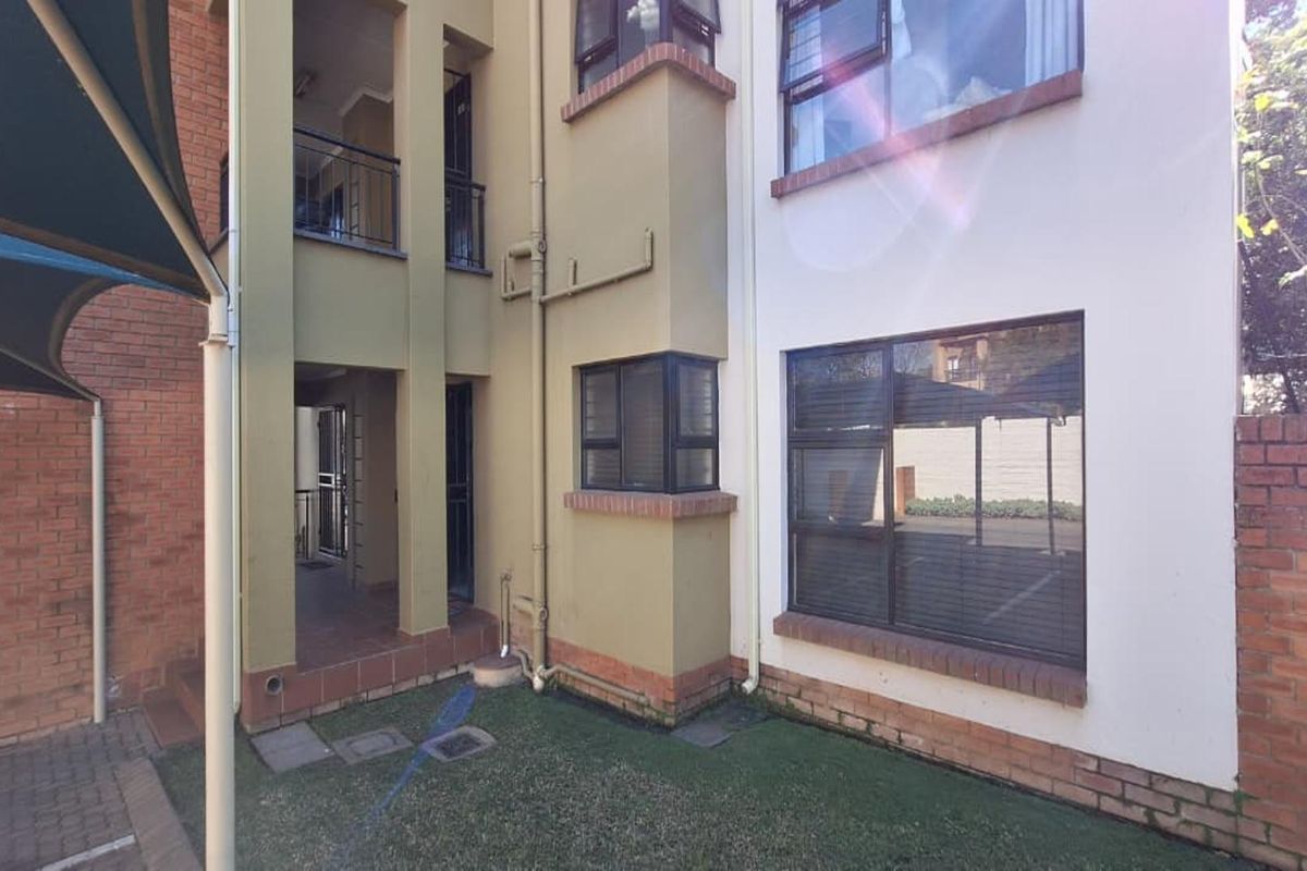 Rear exterior view of the townhouse featuring a combination of brick and painted facade, aluminium window frames, and a small covered patio area.