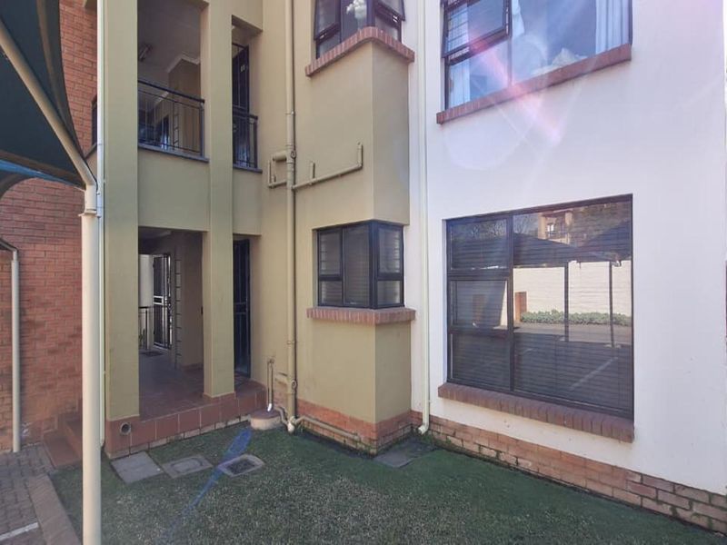 Rear exterior view of the townhouse featuring a combination of brick and painted facade, aluminium window frames, and a small covered patio area.