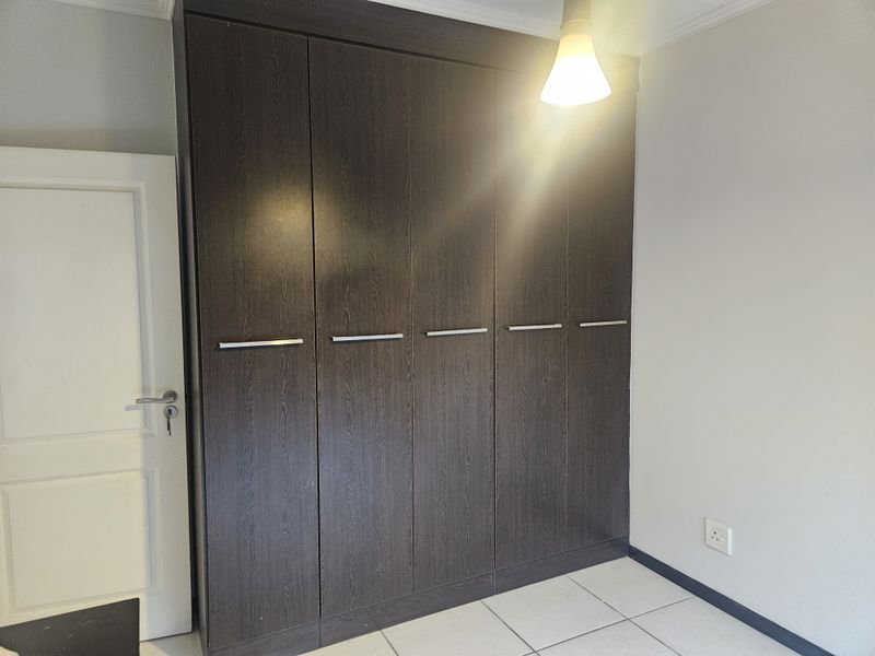 A clean bedroom featuring a large, dark wood-finish built-in wardrobe, neutral walls, and tiled flooring.