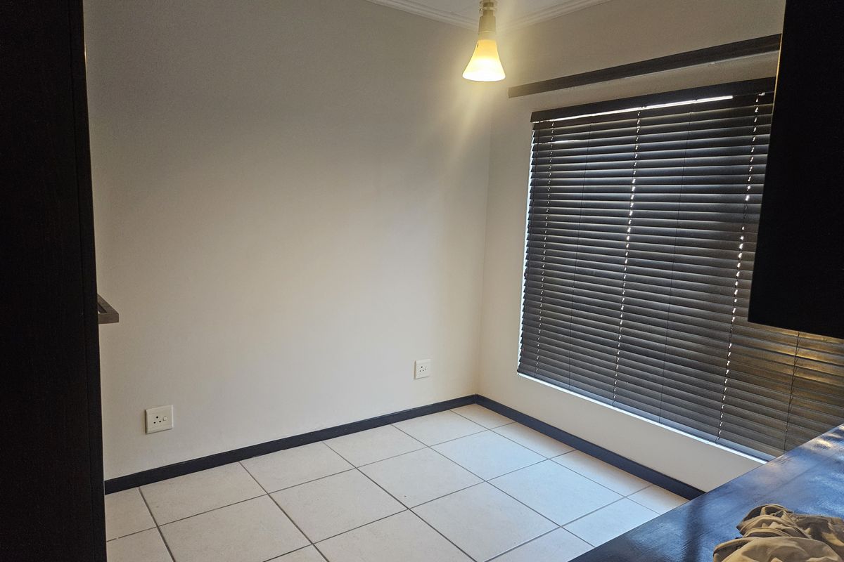 An empty bedroom featuring neutral tiled flooring, dark venetian blinds, and a simple pendant light fixture, offering a blank canvas for personalization.