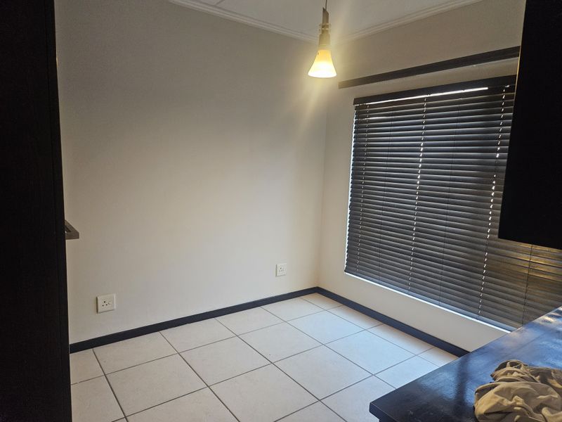 An empty bedroom featuring neutral tiled flooring, dark venetian blinds, and a simple pendant light fixture, offering a blank canvas for personalization.