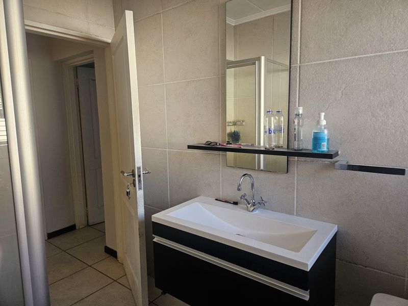 A modern bathroom featuring a sleek vanity cabinet with a basin, wall-mounted mirror, and tiled finishes throughout.