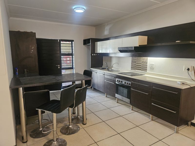 Functional kitchen featuring dark cabinetry, integrated breakfast bar, built-in oven, electric hob, and tiled flooring with direct access to an exterior door.