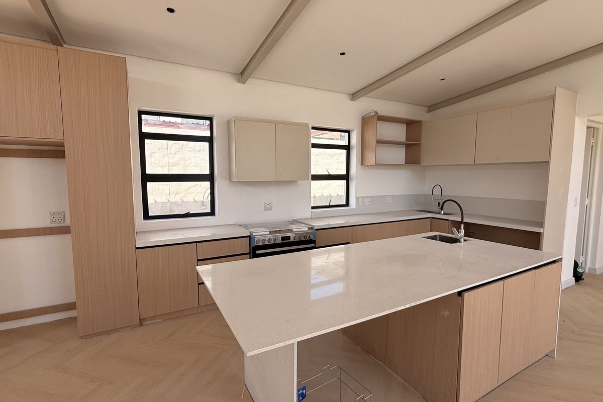 Modern kitchen featuring light wood cabinetry, quartz countertops, a central island, and herringbone flooring in a bright, open-plan layout.