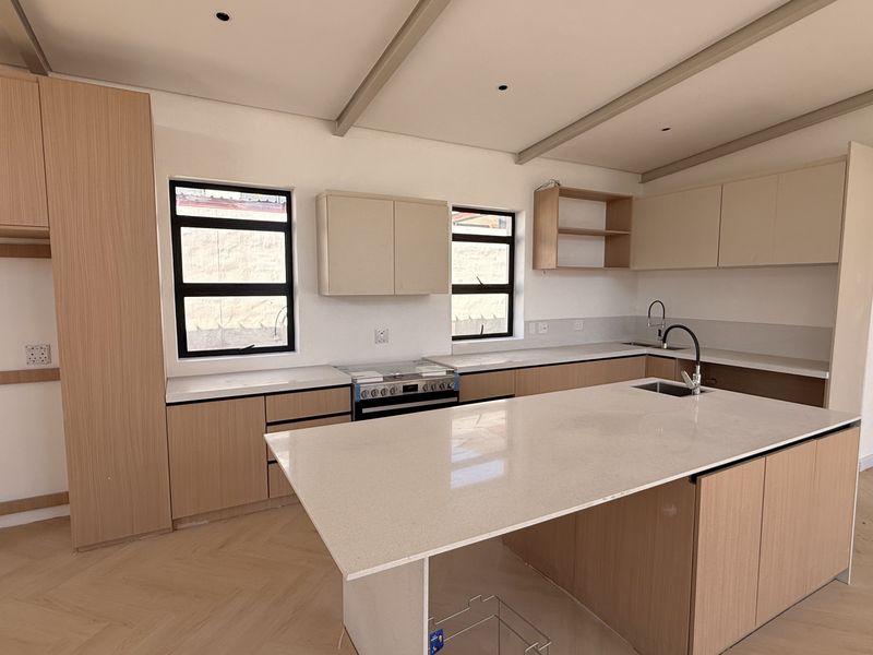 Modern kitchen featuring light wood cabinetry, quartz countertops, a central island, and herringbone flooring in a bright, open-plan layout.