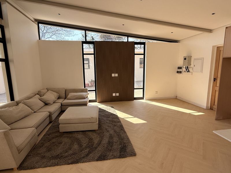 Spacious open-plan living area featuring modern herringbone timber flooring, large windows with natural light, and contemporary timber feature wall paneling.
