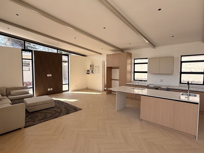 Spacious open-plan living and kitchen area featuring modern herringbone timber flooring, sleek cabinetry, a central island, and abundant natural light from clerestory windows.
