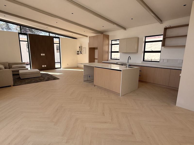 Spacious open-plan living and kitchen area featuring modern light wood cabinetry, a central island, herringbone flooring, and high clerestory windows for natural light.