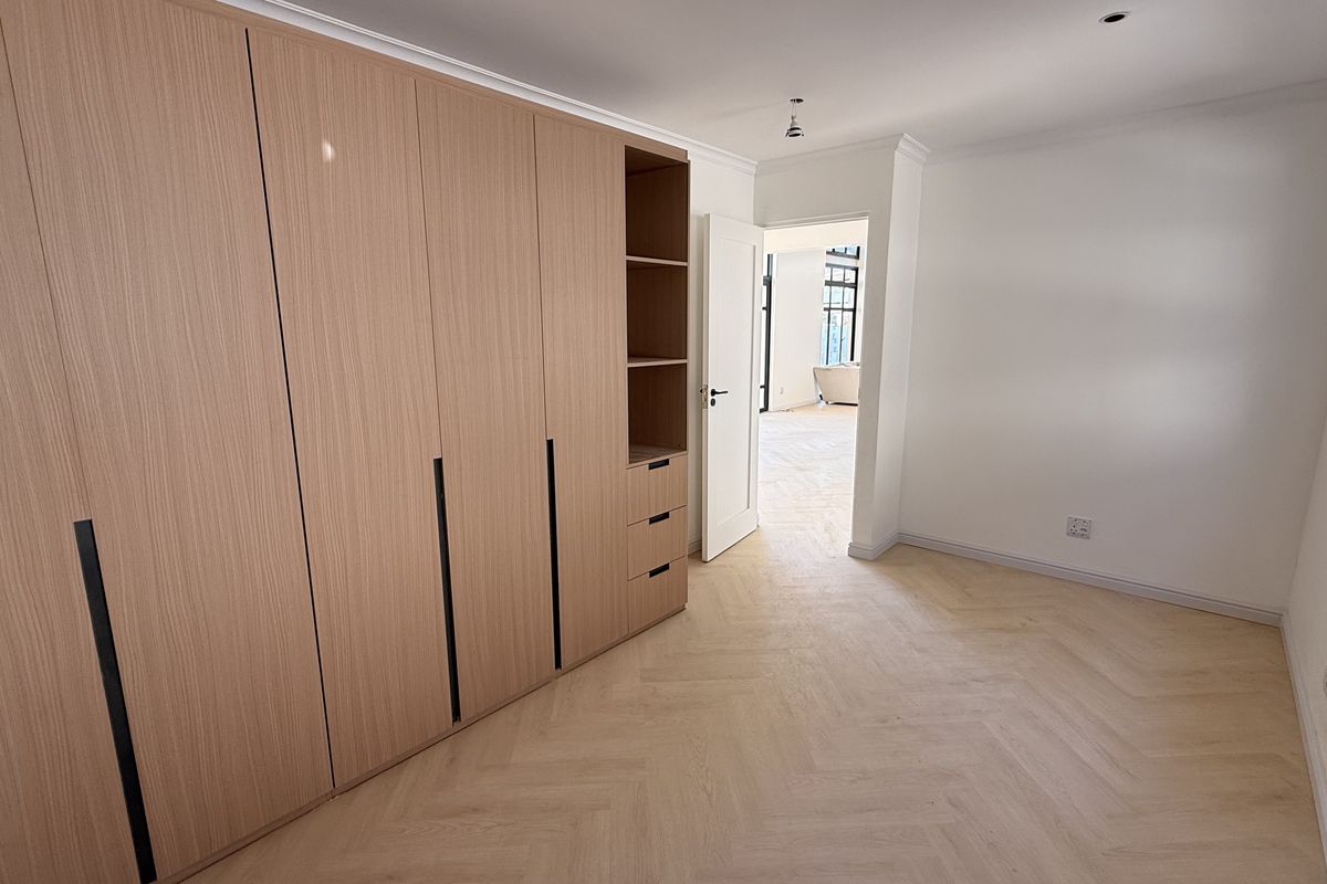 A bright, modern bedroom featuring light wood herringbone flooring and extensive built-in cabinetry with integrated shelving.