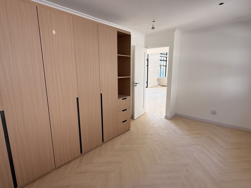 A bright, modern bedroom featuring light wood herringbone flooring and extensive built-in cabinetry with integrated shelving.