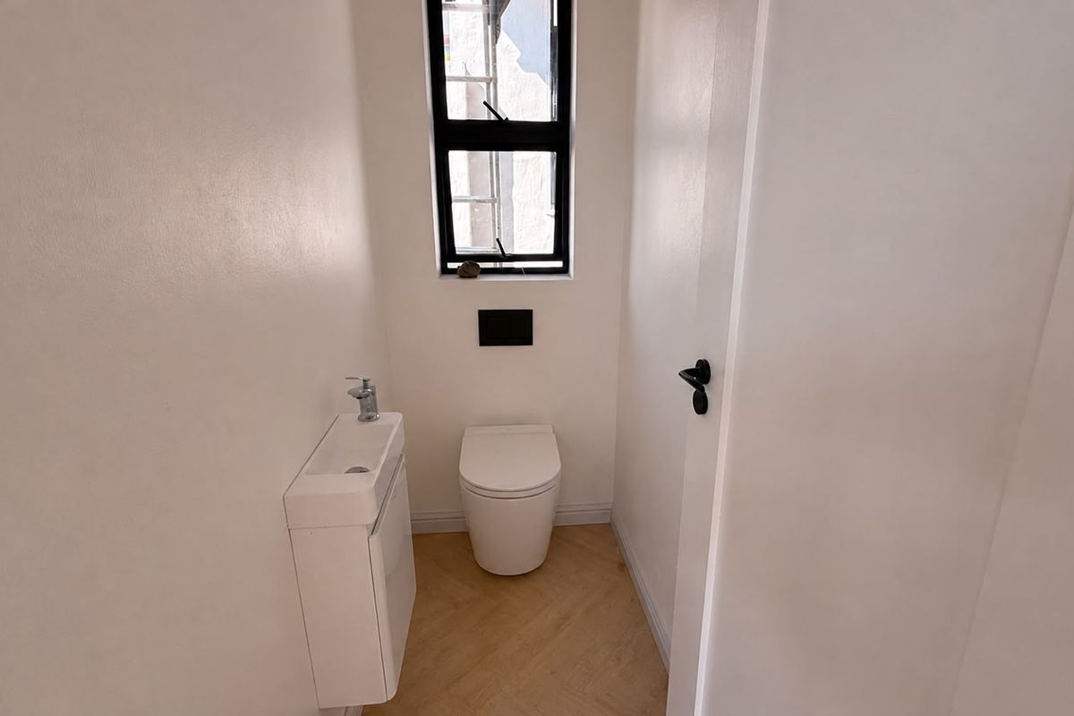 A modern, compact powder room featuring a wall-hung toilet, sleek vanity basin, and stylish herringbone flooring with a neutral color palette.