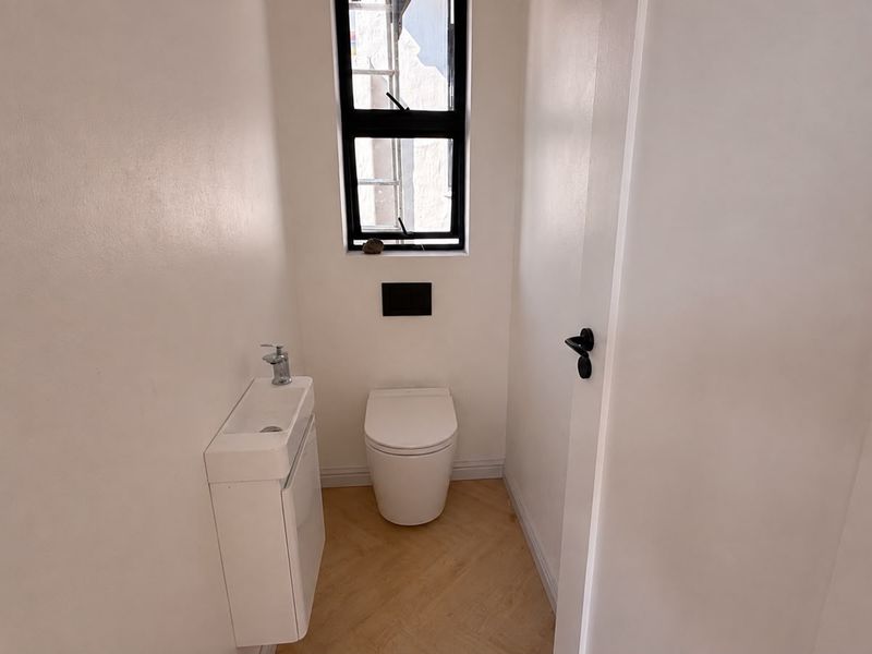 A modern, compact powder room featuring a wall-hung toilet, sleek vanity basin, and stylish herringbone flooring with a neutral color palette.