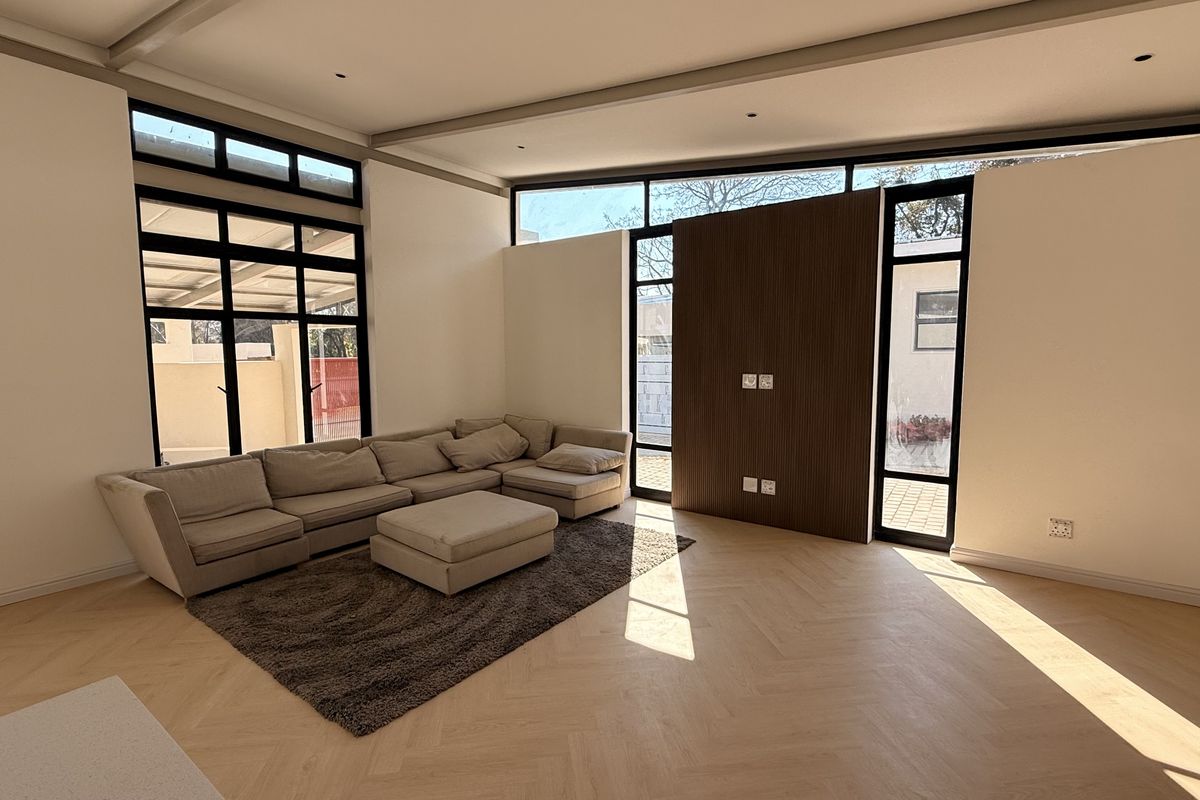 Spacious living room featuring elegant herringbone timber flooring, a modern timber feature wall, and expansive floor-to-ceiling windows that provide abundant natural light.