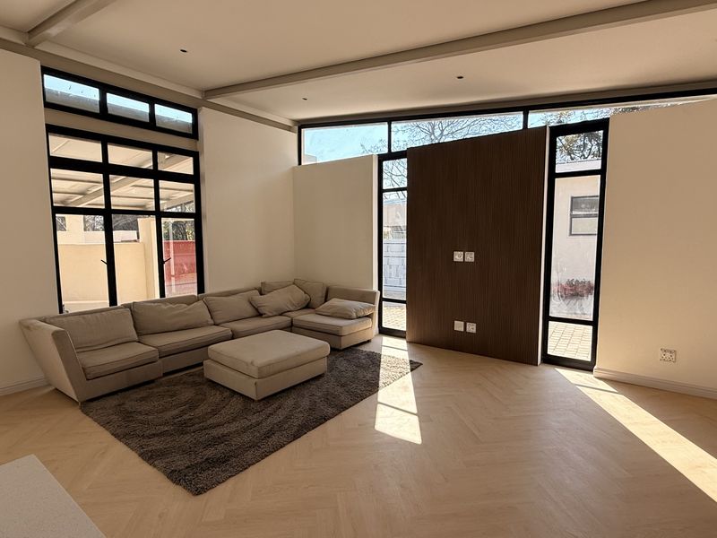Spacious living room featuring elegant herringbone timber flooring, a modern timber feature wall, and expansive floor-to-ceiling windows that provide abundant natural light.