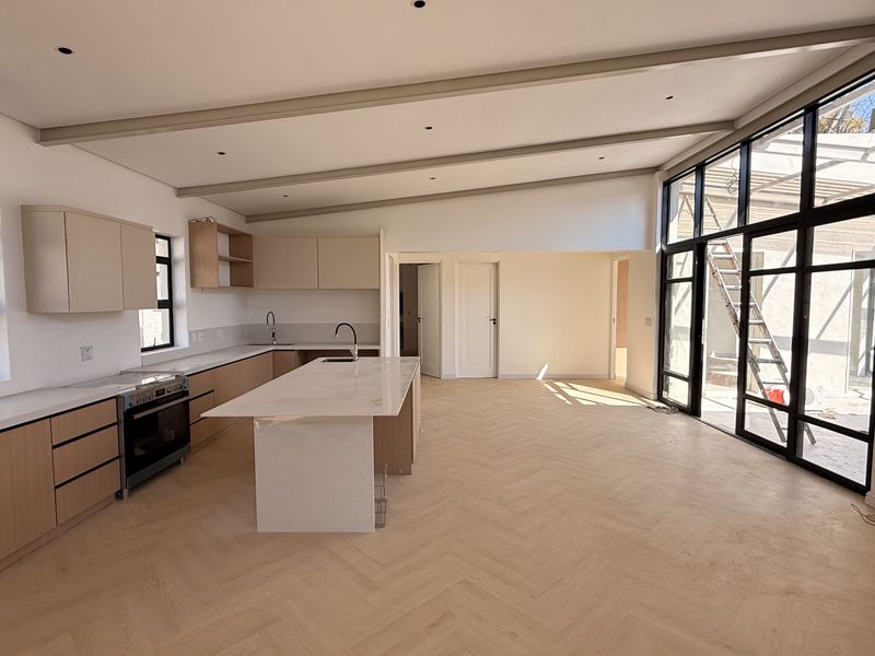 Spacious open-plan kitchen and living area featuring modern cabinetry, a central island, herringbone timber flooring, and large glass doors leading to the exterior.