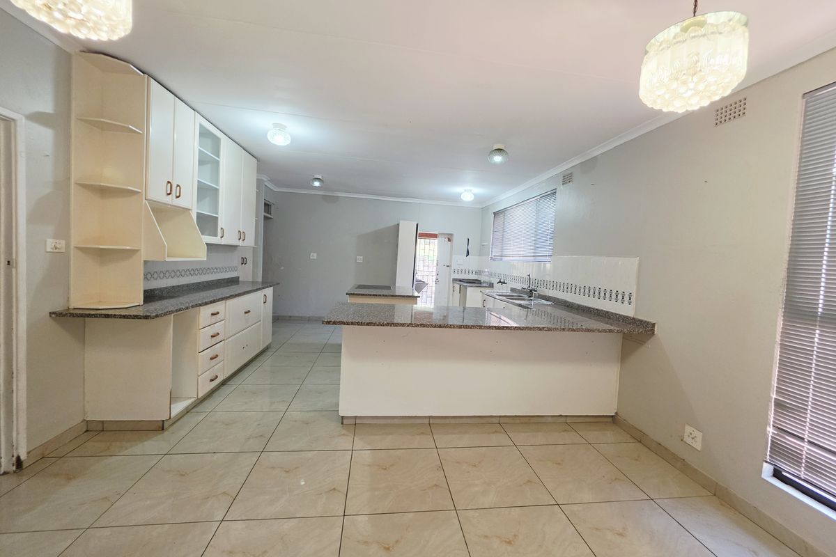 Spacious kitchen featuring granite countertops, ample built-in cabinetry, tiled flooring, and a functional layout with a breakfast bar area.