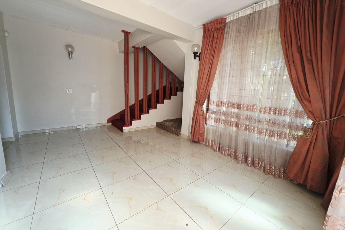 Spacious living area featuring large format floor tiles and a staircase with a wooden balustrade, offering a blank canvas for interior design.