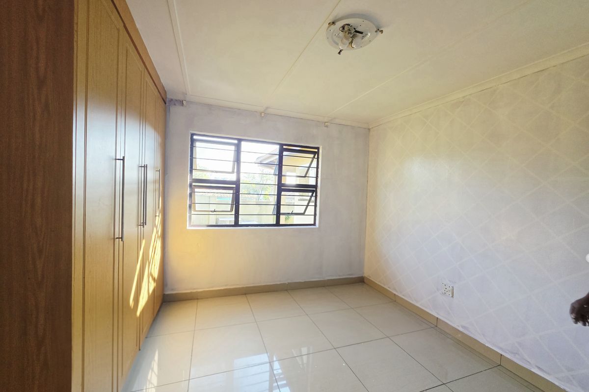 A vacant bedroom featuring built-in wooden cupboards, tiled flooring, and a window with security bars.