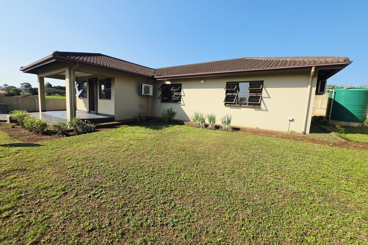 Rear view of the house featuring a covered patio, louvered windows, and a large water storage tank set within a grassed garden area.