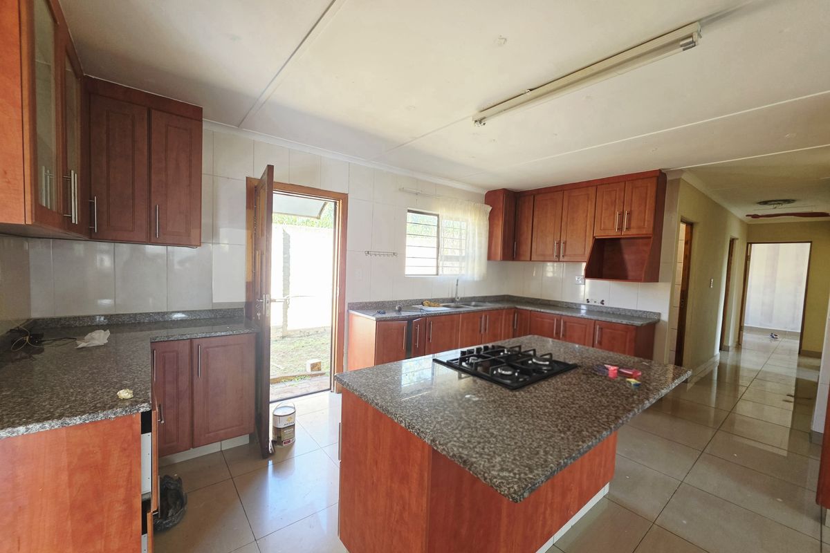 Spacious kitchen featuring granite countertops, wooden cabinetry, a central island with a gas hob, and direct access to the rear exterior.