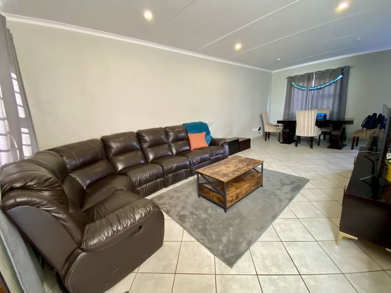 Spacious open-plan living and dining area featuring neutral wall tones, ceramic tiled flooring, and recessed ceiling lighting.