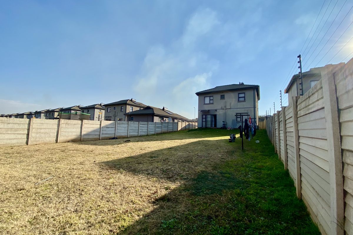 A spacious rear garden featuring a large lawn area enclosed by precast concrete boundary walls with integrated electric fencing.