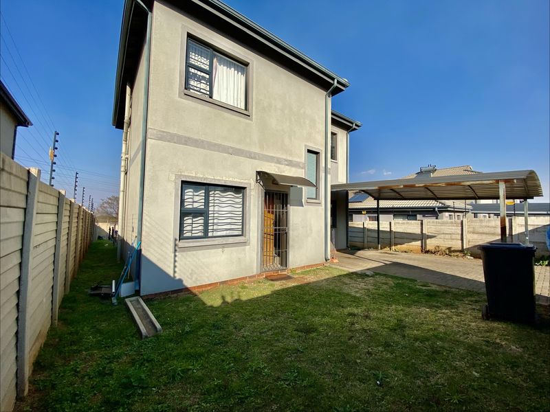 Rear view of the property featuring a paved driveway, carport, and secure boundary walls with electric fencing.