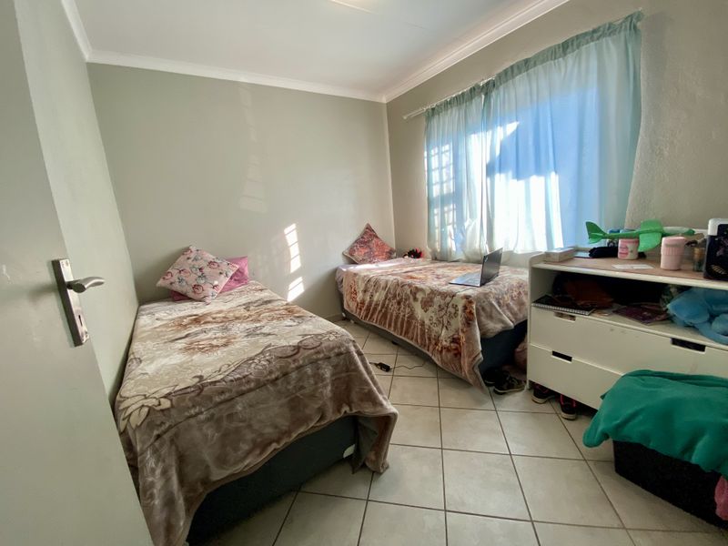 A functional bedroom featuring tiled flooring, coved ceilings, and natural light through a window with curtain rails.