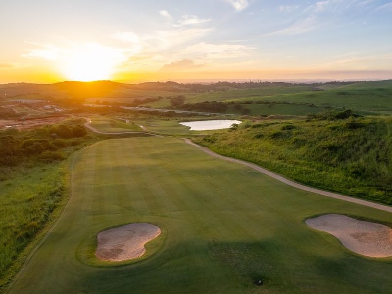 Aerial view of a scenic golf course fairway featuring sand bunkers and a water hazard at sunset.