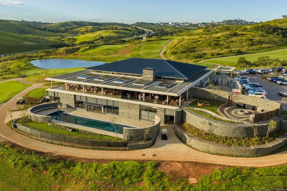 Aerial view of a modern clubhouse featuring a swimming pool, extensive stone masonry, and panoramic views of the surrounding golf course and landscape.