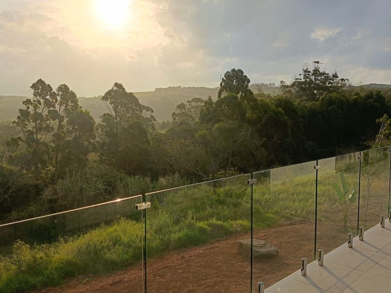 A scenic elevated view overlooking a lush green landscape and forest, featuring a modern glass balustrade and tiled patio area.