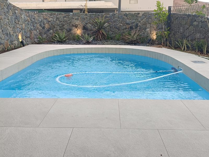 A well-maintained swimming pool area featuring a curved design, modern tiled surround, and a decorative stone retaining wall with integrated garden beds.