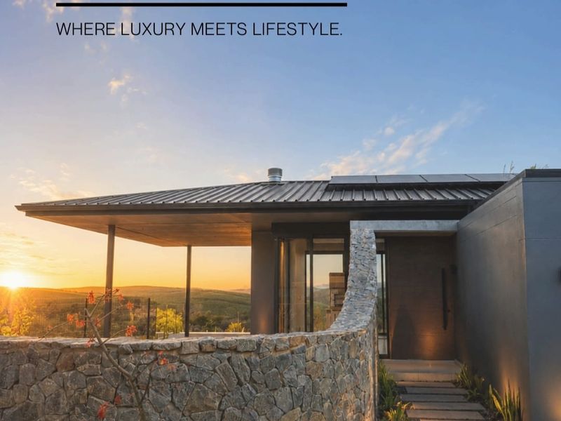 Modern architectural facade featuring stone cladding, a sleek metal roof with solar panels, and a paved walkway leading to the main entrance.