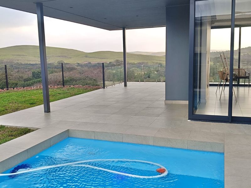 Modern covered patio featuring large format floor tiles, a built-in swimming pool, and seamless glass sliding doors overlooking a scenic landscape.