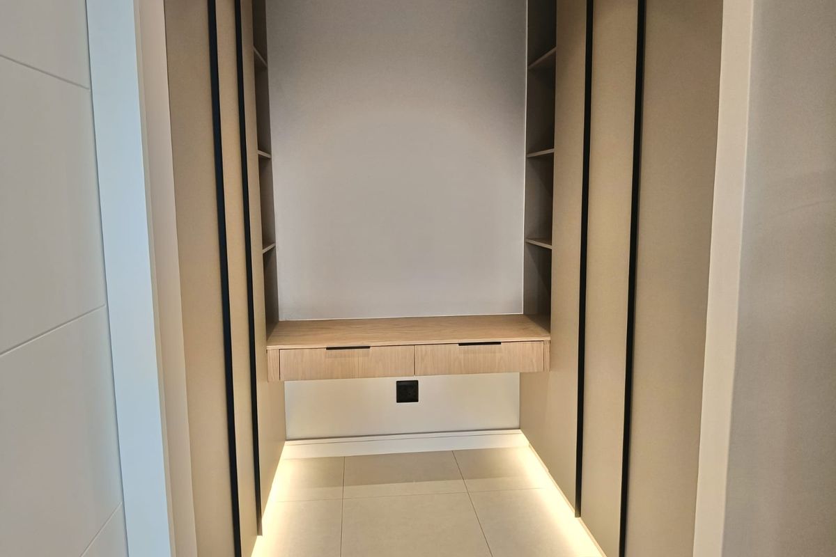 A modern, minimalist built-in dressing area or study nook featuring floating cabinetry, integrated shelving, and ambient under-cabinet LED lighting.