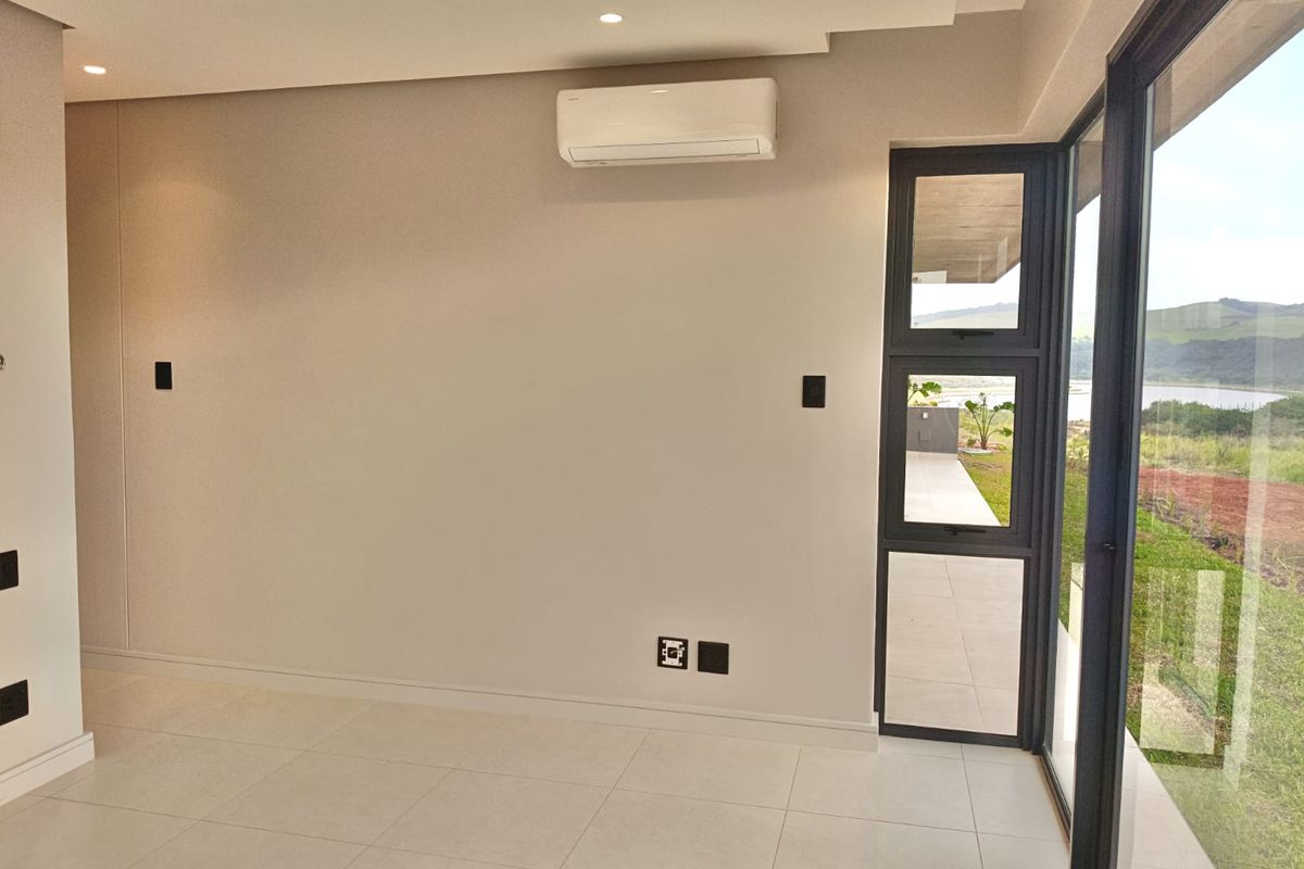 A bright, modern, and empty living area featuring tiled floors, recessed lighting, an air conditioning unit, and large windows with scenic outdoor views.