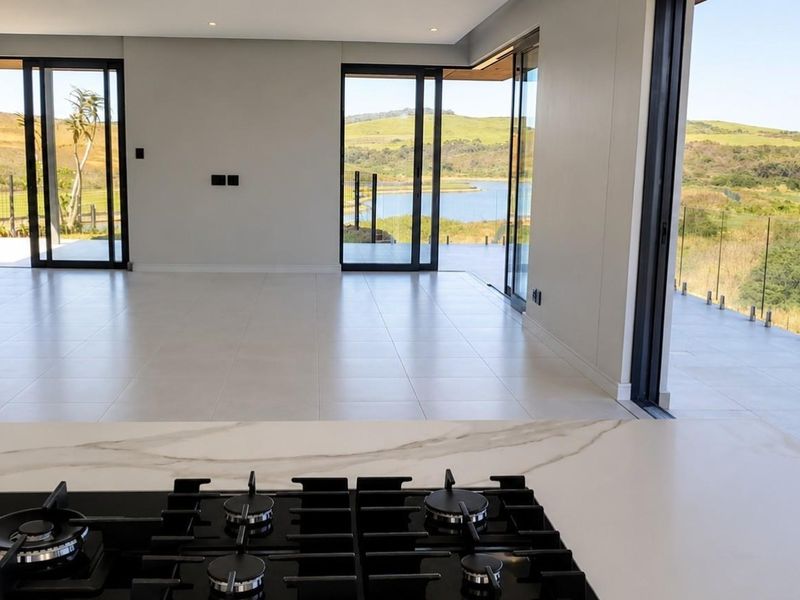 Modern open-plan living area featuring a sleek kitchen island with gas hob, expansive sliding doors, and seamless transition to a balcony with scenic views.
