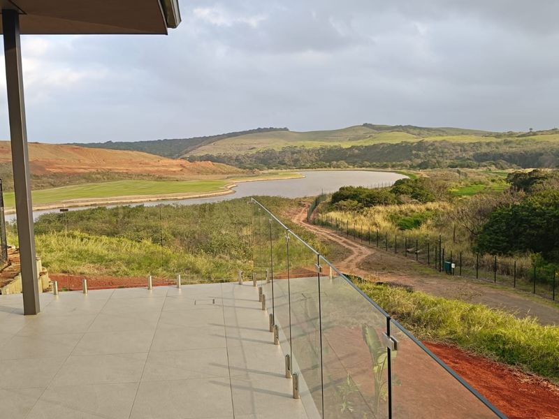 A modern covered patio featuring large format floor tiles and a frameless glass balustrade, offering expansive views of the surrounding landscape and water.