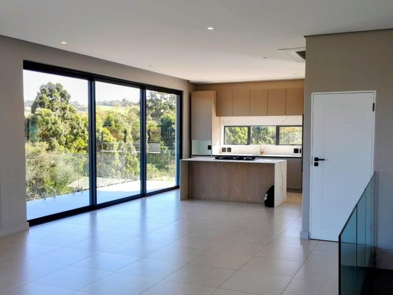 Modern open-plan kitchen and living area featuring sleek cabinetry, a central island with a gas hob, and large sliding doors opening to a balcony.