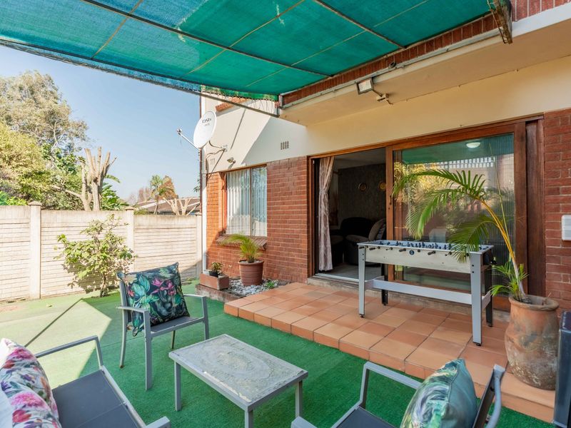 A covered patio area featuring tiled flooring, artificial grass, and direct access to the interior through sliding glass doors.