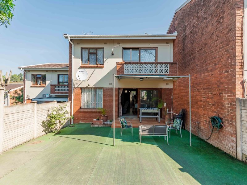 Rear view of the townhouse featuring a paved patio area, metal pergola frame, and a private garden space with boundary walling.