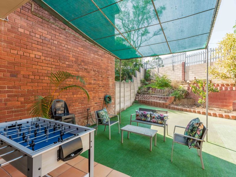 Outdoor patio area featuring a shade cloth canopy, terracotta tiling, and a tiered garden with brick retaining walls.
