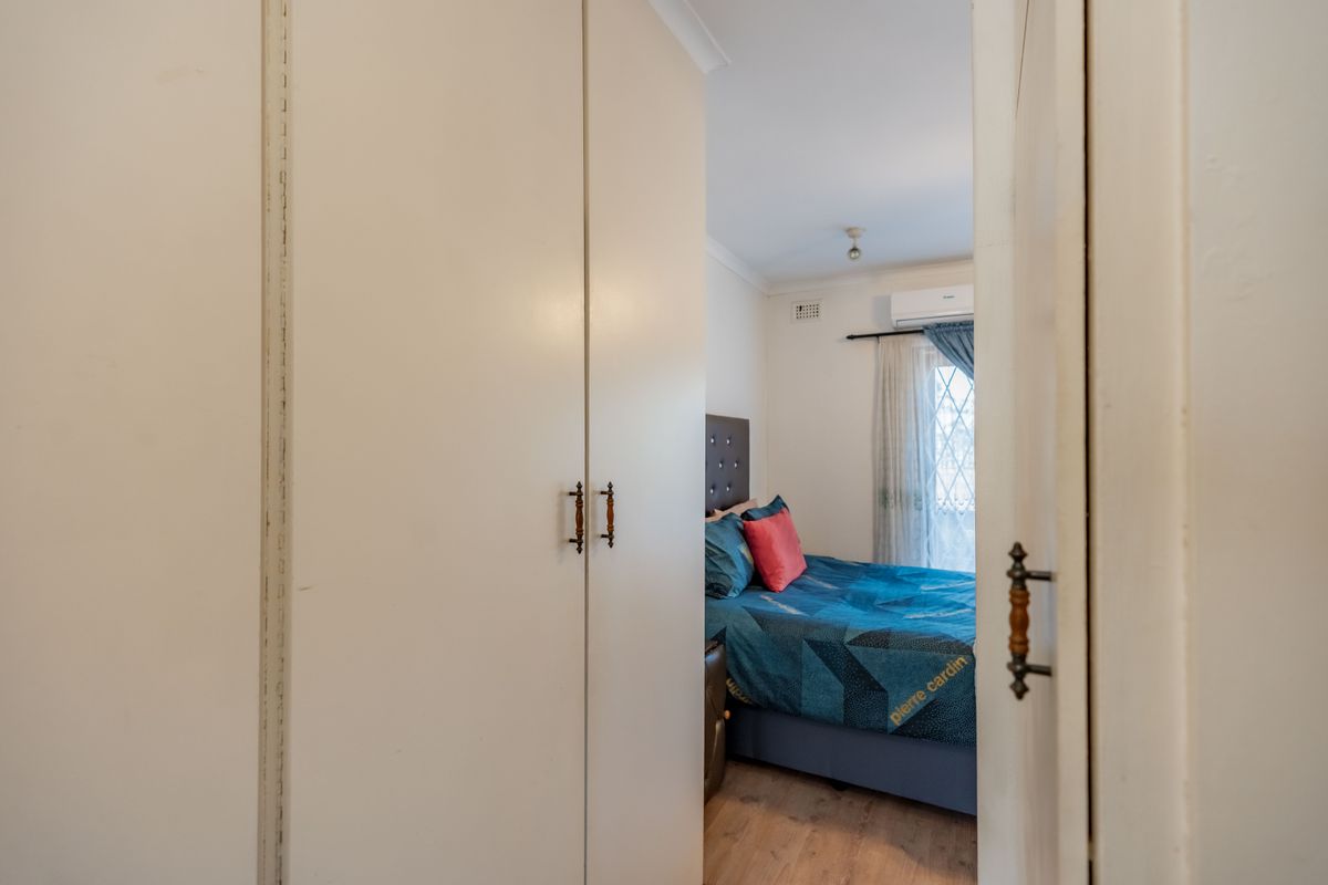 A bedroom featuring built-in cupboards, laminate flooring, and a wall-mounted split-system air conditioner.